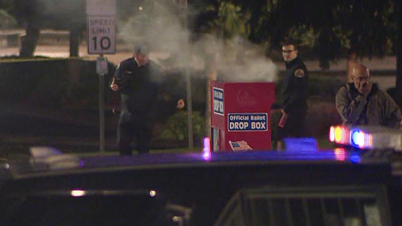 In this image made from a video provided by KGW8, authorities investigate smoke pouring out of a ballot box on Monday, Oct. 28, 2024, in Vancouver, Wash. (KGW8 via AP)