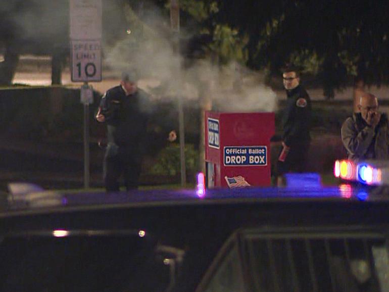 In this image made from a video provided by KGW8, authorities investigate smoke pouring out of a ballot box on Monday, Oct. 28, 2024, in Vancouver, Wash. (KGW8 via AP)