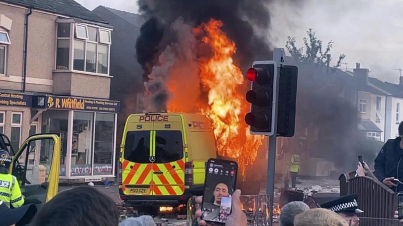 A police van buns as and unruly crowd clashed with police in Southport