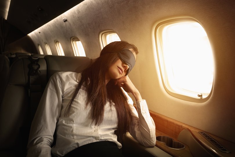 Flight crew uniforms and emblems are generic and are not associated with any particular company. Woman sleeping on plane.