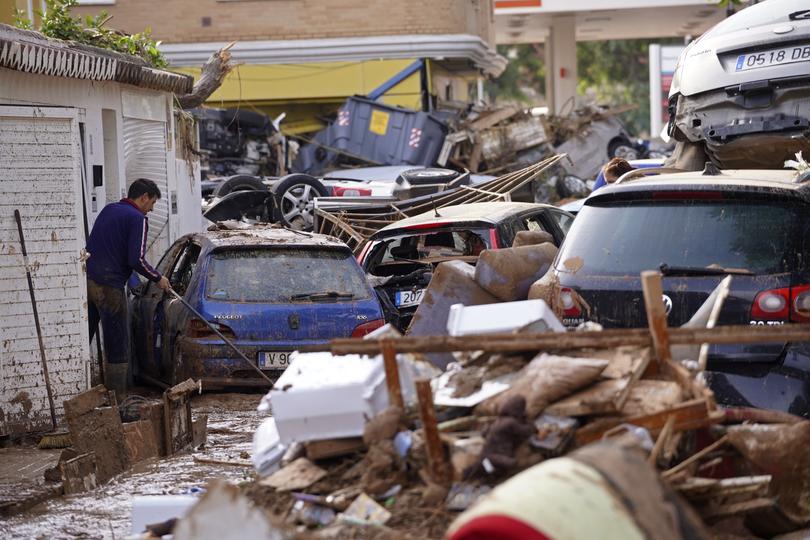 A man sweeps by piled up cars after floods in Massanassa.