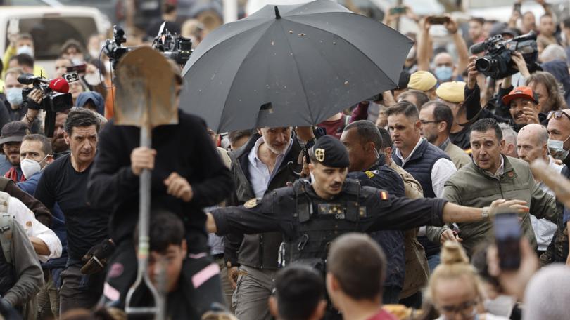 King Felipe of Spain had to be protected by royal guards and umbrellas as locals hurled objects and mud. 