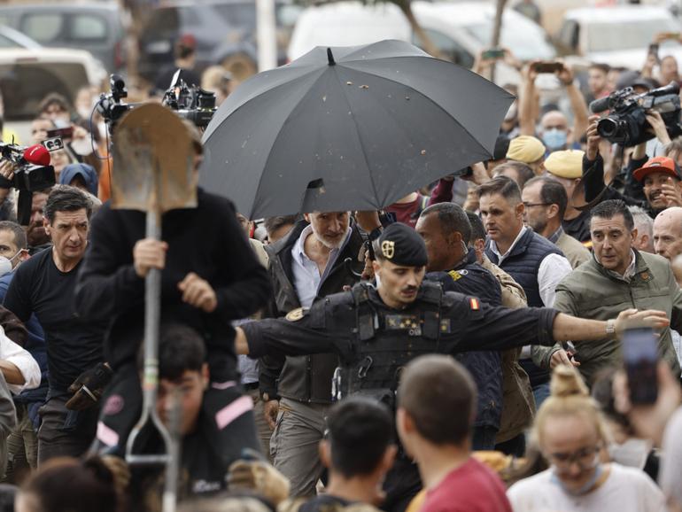 King Felipe of Spain had to be protected by royal guards and umbrellas as locals hurled objects and mud. 