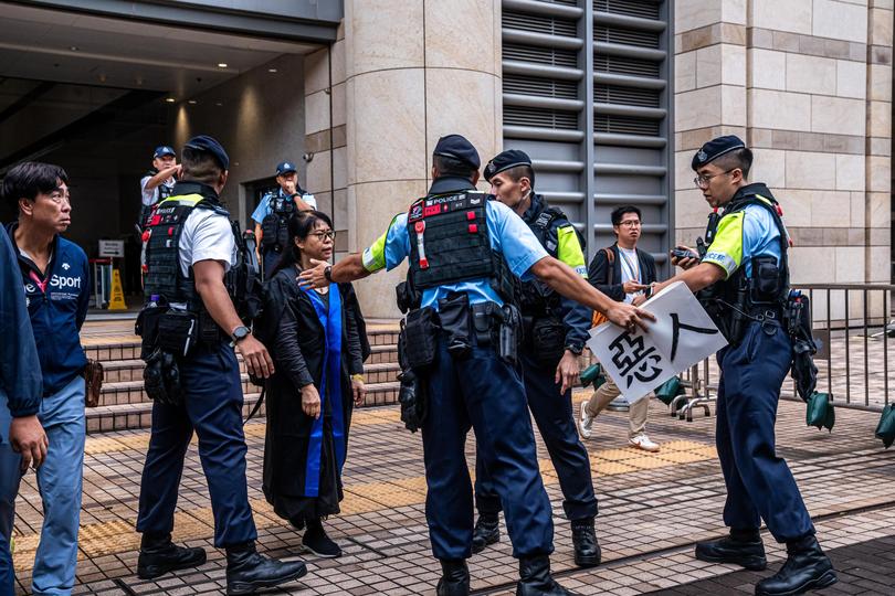 Police officers remove a protest banner from Elsa Wu, the foster mother of one of the defendants Hendrick Lui, as she leaves the West Kowloon Court following a sentencing hearing for 45 pro-democracy activists in Hong Kong, China, on Tuesday, Nov. 19, 2024. 