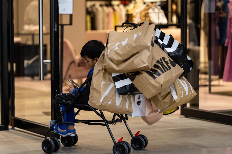 A child waits outside a shop on a trolley full of shopping bags during Black Friday sales in Chadstone.