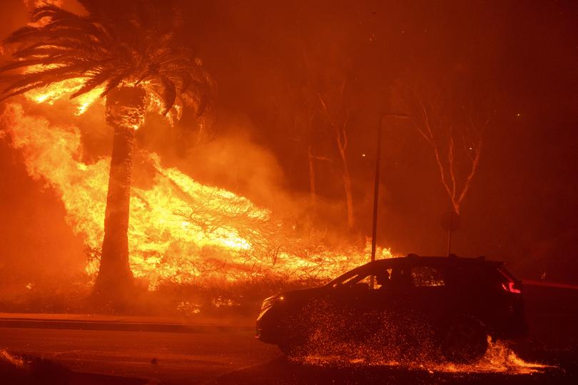 A car drives past flames from the Franklin Fire at Pepperdine University in Malibu, Calif., Tuesday, Dec. 10, 2024.