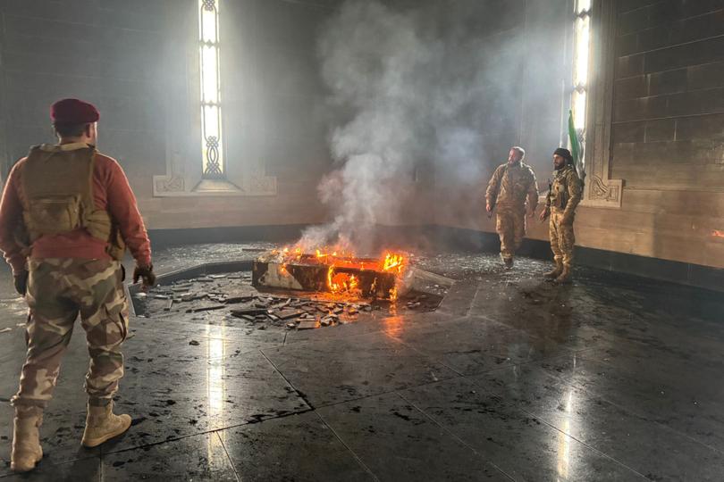 Rebel fighters stand next to the burning gravesite of Syria's late president Hafez al-Assad at his mausoleum in the family's ancestral village of Qardaha.