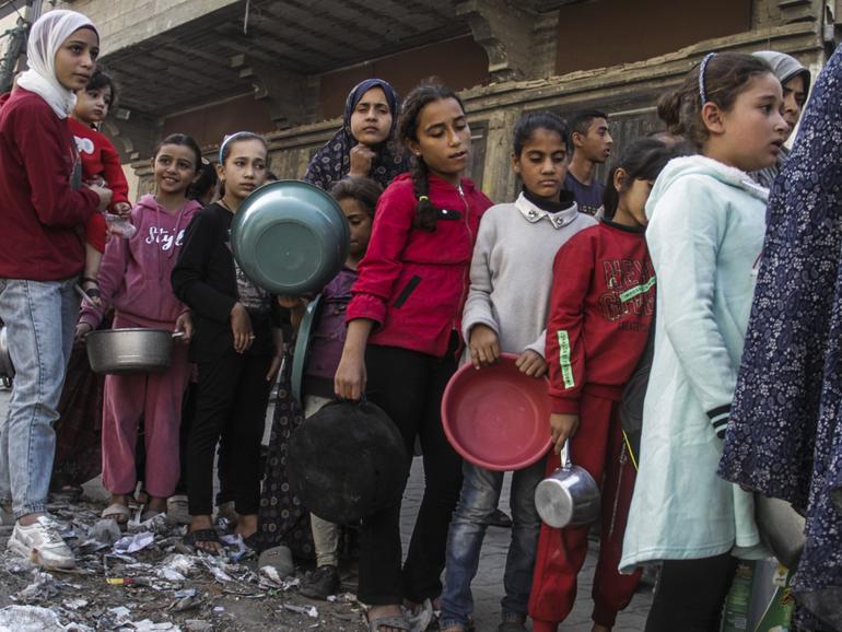 Internally displaced Palestinian children queue to receive food distributed by charitable organisations in the Nasser neighborhood of Gaza City.