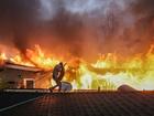 Steve Salinas shields himself from intense heat as he hoses down a neighbours rooftop on Sinaloa Ave. as the Eaton Fire continues to grow.