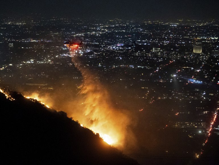 Water is dropped by helicopter on the burning Sunset Fire in the Hollywood Hills section of Los Angeles, Wednesday, Jan. 8, 2025. (AP Photo/Ethan Swope)