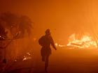 PACIFIC PALISADES, CALIFORNIA - JANUARY 07: A photographer runs past burnng houses after taking a photo on January 7, 2025 in Pacific Palisades, Los Angeles, California. Over 30,000 were ordered to evacuate in Southern California areas as Santa Anna winds swept through the region. The high population, drought conditions, abundant fuel, and mountain wind strength have created a high-fire danger environment that has the potential to spread. (Photo by Michael Nigro/Sipa USA)