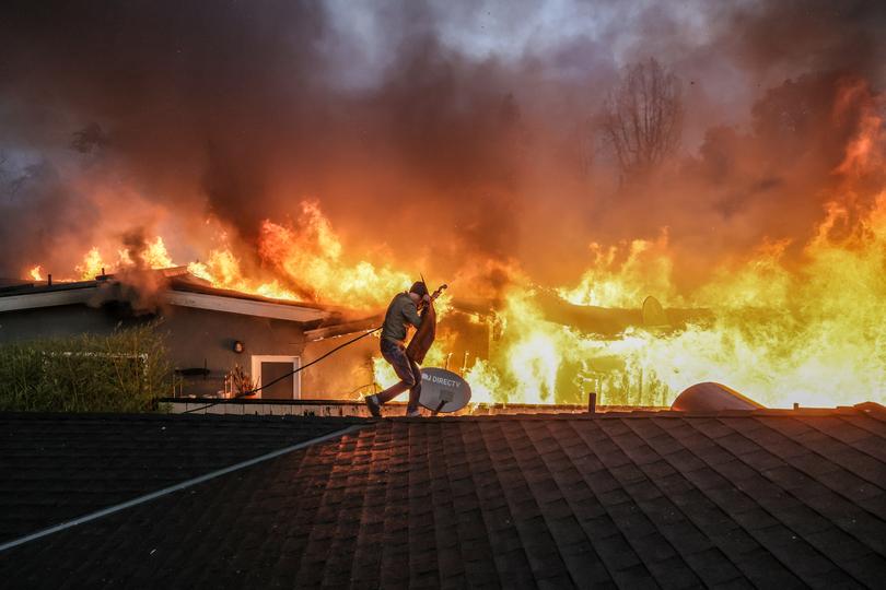 Altadena, CA, Wednesday, Jan 8, 2025 - Steve Salinas shields from intense heat as he hoses down a neighbours rooftop on Sinaloa Ave. as the Eaton Fire continues to grow.