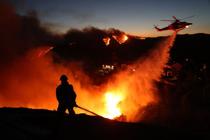 Fire personnel respond to homes destroyed while a helicopter drops water as the Palisades Fire grows in Pacific Palisades, California on January 7, 2025.