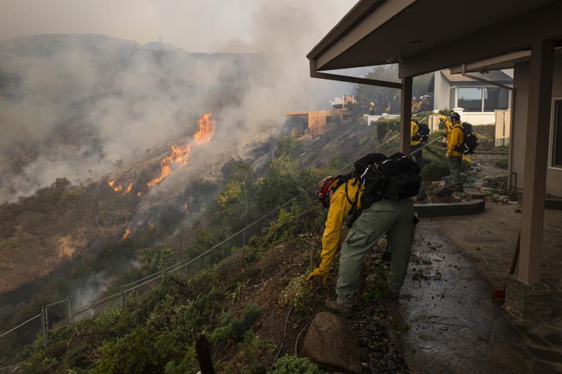 Monterey County Firefighters clear shrubbery around Brentwood residences as the Palisades Fire grows closer.