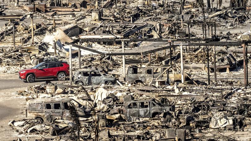 A car drives past homes and vehicles destroyed by the Palisades Fire at the Pacific Palisades Bowl Mobile Estates.