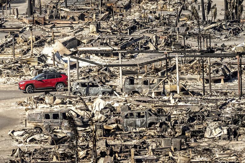 A car drives past homes and vehicles destroyed by the Palisades Fire at the Pacific Palisades Bowl Mobile Estates on Sunday, Jan. 12, 2025, in Los Angeles.