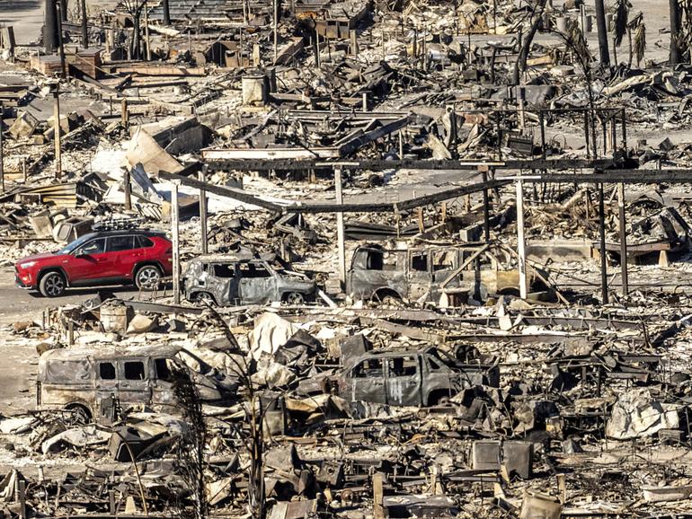 A car drives past homes and vehicles destroyed by the Palisades Fire.