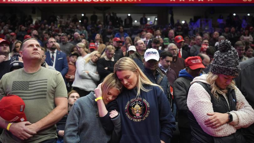 Supporters of President Donald Trump bow their heads during the invocation while watching inauguration ceremonies taking place at the U.S. Capitol on screens at Capitol One Arena in Washington, Monday, Jan. 20, 2025. (AP Photo/Mark Schiefelbein)