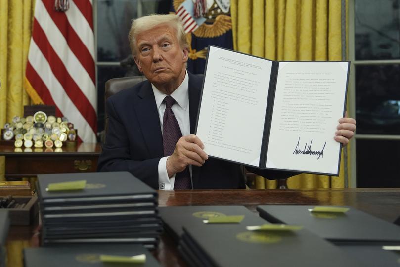 President Donald Trump holds up an executive order commuting sentences for people convicted of January 6 offences.