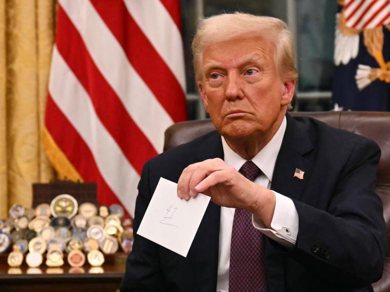 US President Donald Trump holds up outgoing President Joe Biden's letter as he signs executive orders in the Oval Office.