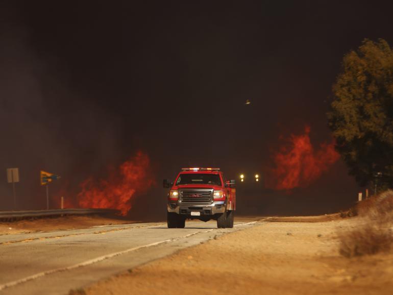 A fire truck drives past flames caused by the Hughes Fire in Castaic, Calf., Wednesday, Jan. 22, 2025. (AP Photo/Ethan Swope)