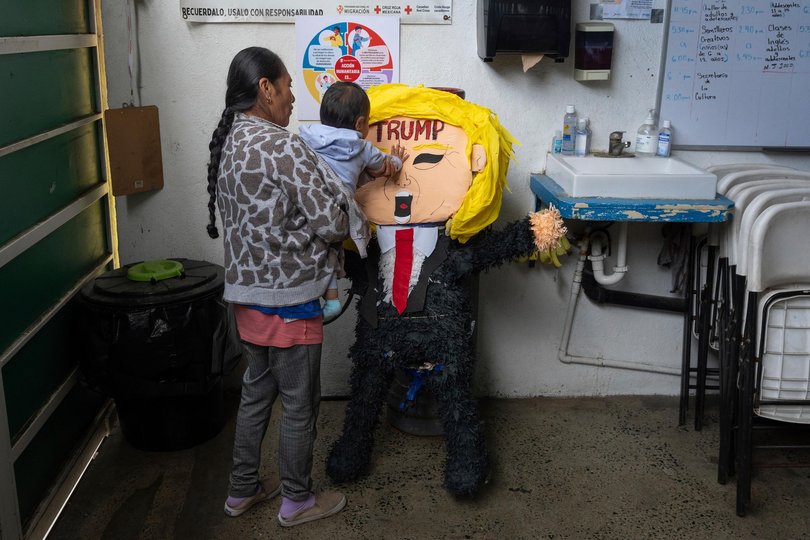 A migrant woman from the Mexican state of Guerrero holds her 1-year-old granddaughter as she hits a piñata of President Donald Trump at a shelter for migrants on Wednesday.