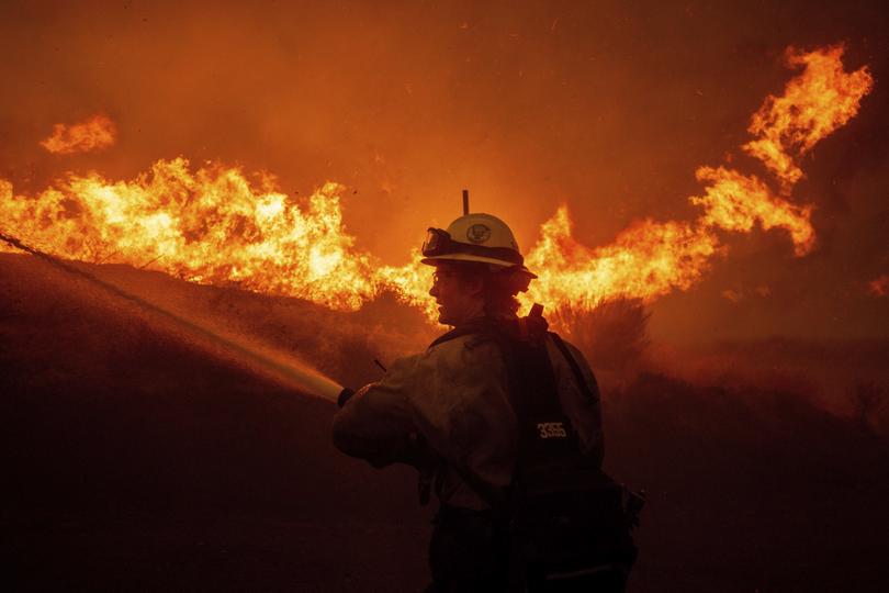 A firefighters spray water as he monitor flames caused by the Hughes Fire along a roadside in Castaic, Calf., Wednesday, Jan. 22, 2025. (AP Photo/Ethan Swope)