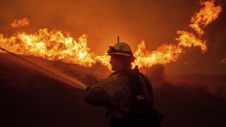 A firefighter sprays water as he monitors flames caused by the Hughes Fire along a roadside in Castaic, Calf.