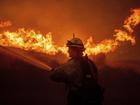 A firefighter sprays water as he monitors flames caused by the Hughes Fire along a roadside in Castaic, Calf.