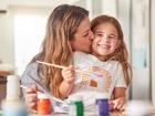 Mother, child and painting art in home using paint brush for creative activity for learning, bonding and love between mom and daughter. Woman or parent give girl kid kiss for creativity in USA house.