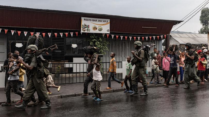 Members of the M23 armed group walk alongside residents through a street of the Keshero neighborhood in Goma.