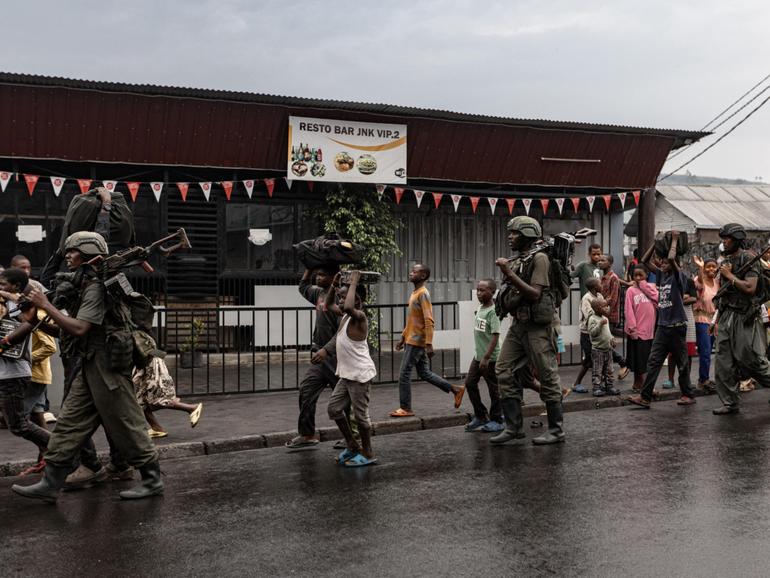 Members of the M23 armed group walk alongside residents through a street of the Keshero neighborhood in Goma.