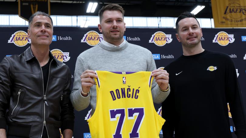 Luka Doncic (C) of the Los Angeles Lakers holds his new jersey while standing alongside general manager Rob Pelinka (L) and head coach JJ Redick (R).