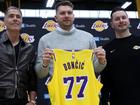 Luka Doncic (C) of the Los Angeles Lakers holds his new jersey while standing alongside general manager Rob Pelinka (L) and head coach JJ Redick (R).