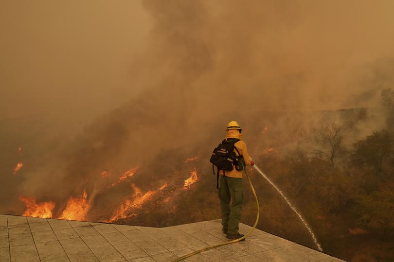 A firefighter hoses down flames as the Palisades Fire approaches in Mandeville Canyon.