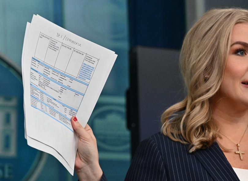 White House press secretary Karoline Leavitt, on Feb. 12, holds an example of a government contract that she said DOGE identified as violating the president's policies. 