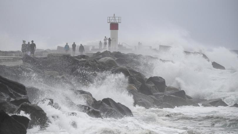 Waves crash onto rocks as people look on at the Spit, on the Gold Coast. Waves of 4 metres have been pummelling the coast.