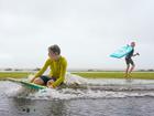 Two boys use their boogie boards on a flooded patch of grass in Scarborough, Brisbane.