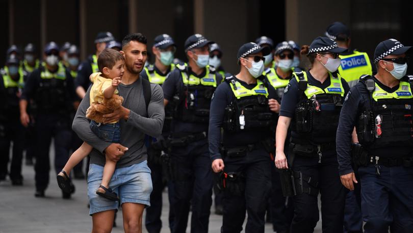 A man holding a child walks Victoria Police as people participate in the Eureka Freedom Rally anti-vaccination and anti-mandatory vaccination protest in Melbourne, Saturday, December 4, 2021.