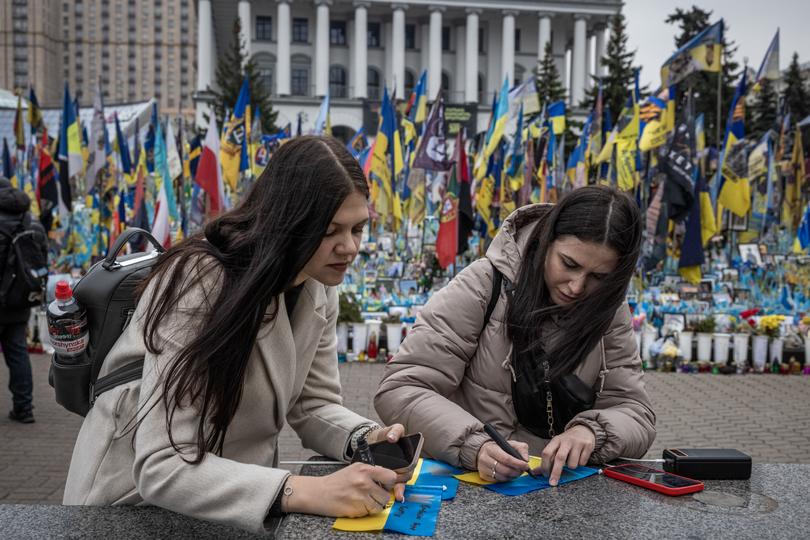 Oksana Harei, left, and Karina Harei write notes on flags at a makeshift memorial for soldiers in Kyiv’s Maidan on Wednesday. 