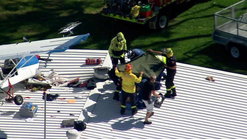 A light plane has crashed into the roof of a building near Sydney, leaving a pilot trapped in the wreckage as emergency services use a cherry picker to reach the man. 7NEWS