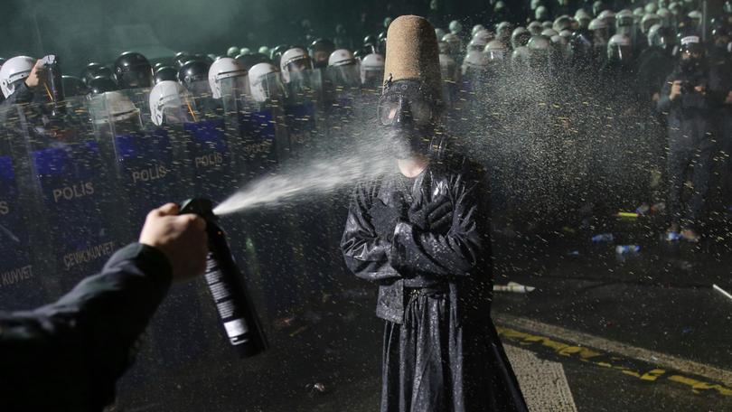 Riot police officers use pepper spray to clear a protester during a protest.