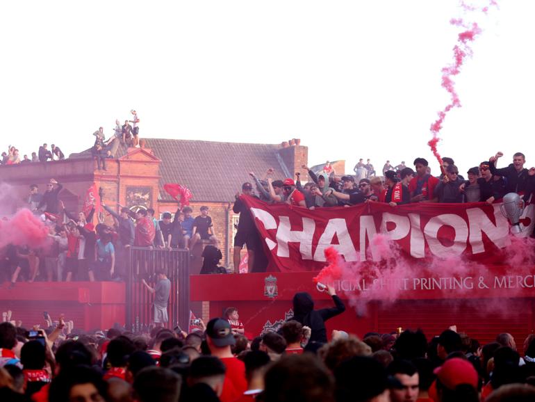 Fans of Liverpool hold up a banner which reads "Champions", while standing on top of a merchandise stand.