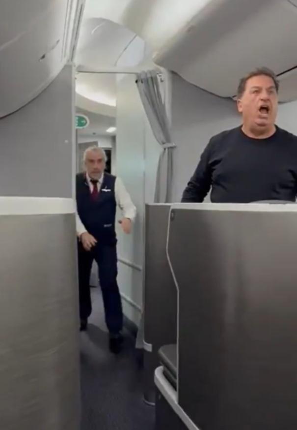The male passenger stands up and starts shouting angrily at the woman in Portuguese to “shut up.”
