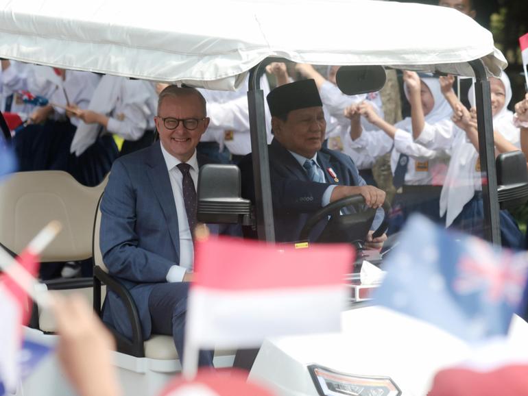 Prime Minister Anthony Albanese rides on a golf cart with Indonesian President Prabowo Subianto.