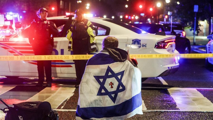 A man draped with an Israeli flag sits where two people were killed near the Capital Jewish Museum.
