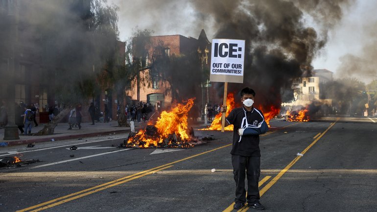 An activist holds a sign as cars burn during protests sparked by immigration raids in Los Angeles, California, USA.