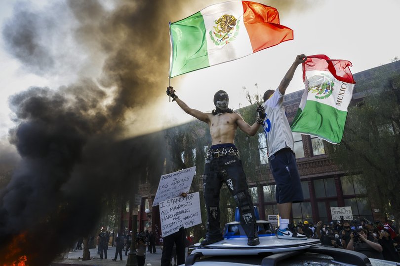 Activists hold aloft Mexican flags as cars burn during protests sparked by immigration raids in Los Angeles, California, USA, 08 June 2025.