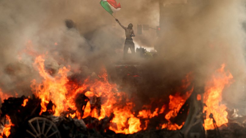 A man waves a Mexican flag as smoke and flames rise from a burning vehicle during a protest against federal immigration sweeps.