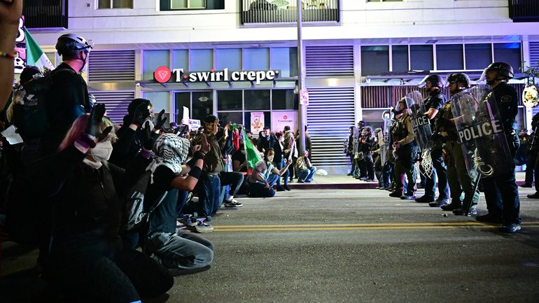 Protesters kneel in the street facing a row of police in riot gear during a protest in response to federal immigration operations in the Little Tokyo neighborhood of downtown Los Angeles, on June 9, 2025. President Donald Trump's administration said on June 9 that it was sending 700 US Marines and thousands more National Guard troops to Los Angeles, sparking a furious response from California's governor over the "deranged" deployment. Protests in Los Angeles, home to a large Latino population, broke out on June 6, triggered by immigration raids that resulted in dozens of arrests of what authorities say are illegal migrants and gang members. (Photo by Frederic J. Brown / AFP)